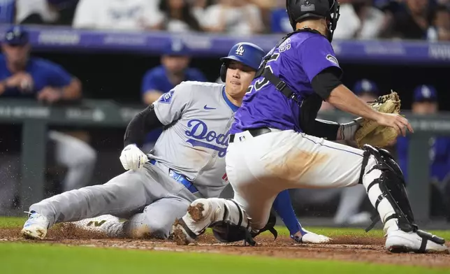 Los Angeles Dodgers' Shohei Ohtani, left, slides safely into home plate to score on a double hit by Kevin Kiermaier as Colorado Rockies catcher Jacob Stallings turns to apply a late tag in the eighth inning of a baseball game Friday, Sept. 27, 2024, in Denver. (AP Photo/David Zalubowski)