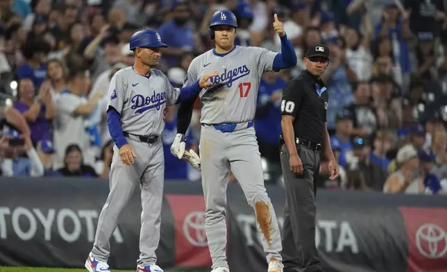 Los Angeles Dodgers third base coach Dino Ebel, left, congratulates Shohei Ohtani after he stole second base and advanced to third base on a throwing error by Colorado Rockies catcher Jacob Stallings in the second inning of a baseball game, Friday, Sept. 27, 2024, in Denver. (AP Photo/David Zalubowski)