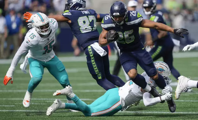 Miami Dolphins safety Jevon Holland (8) tackles Seattle Seahawks running back Zach Charbonnet (26) during the first half of an NFL football game Sunday, Sept. 22, 2024, in Seattle. Miami Dolphins linebacker Jaelan Phillips (15) looks on at left. (AP Photo/Stephen Brashear)