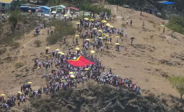 People display a East Timor national flag to show it to Pope Francis taking off with his flight from Díli, East Timor and bound to Singapore, Wednesday, Sept. 11, 2024. The Vatican says some 600,000 people have attended Pope Francis' Mass in East Timor, or nearly half the country's population, on Tuesday on the same field where St. John Paul II prayed in 1989 during the nation's fight for independence from Indonesia. (AP Photo/Gregorio Borgia)