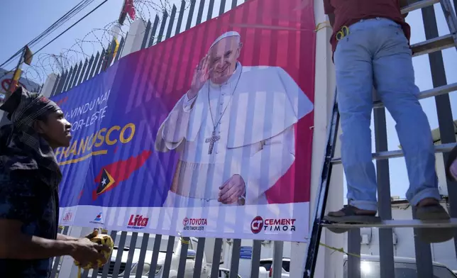 Workers put up a banner to welcome Pope Francis ahead of his visit to East Timor in Dili, Saturday, Sept. 7, 2024. (AP Photo/Dita Alangkara)