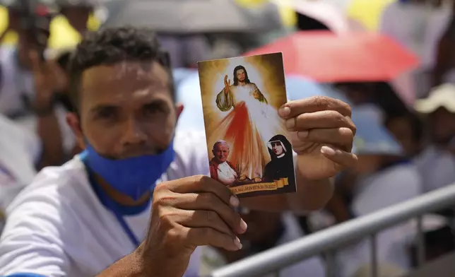 A faithful holds up a postcard as he waits in Tacitolu park for Pope Francis' Mass in Dili, East Timor, Tuesday, Sept. 10, 2024. (AP Photo/Dita Alangkara)