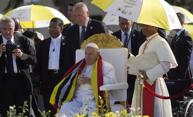 Archbishop of Dili Cardinal Virgilio do Carmo da Silva, right, protects Pope Francis, wearing an East Timor traditional scarf, from the sun with an umbrella with the colors of the Vatican flag as he arrives to preside over a votive mass of the Blessed Virgin Mary Queen in Tasitolu, some 8 kilometers west of Dili, East Timor, Tuesday, Sept. 10, 2024. Pope Francis presides over a mass in a seaside park on the same field where St. John Paul II celebrated a historic liturgy during East Timor's fight for independence from Indonesian rule. (AP Photo/Gregorio Borgia)