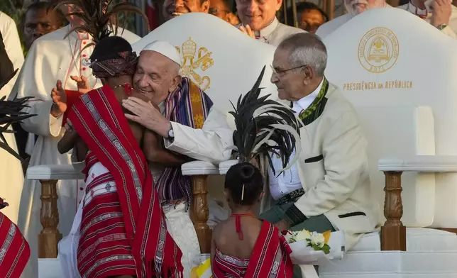 Pope Francis hughs a child in traditional dress as he attends with East Timor's President José Manuel Ramos-Horta, seated at right, a welcome ceremony outside the Presidential Palace in Dili, East Timor, Monday, Sept. 9, 2024. Pope Francis arrived in East Timor on Monday to encourage its recovery from a bloody and traumatic past and celebrate its development after two decades of independence from Indonesian rule. (AP Photo/Gregorio Borgia)