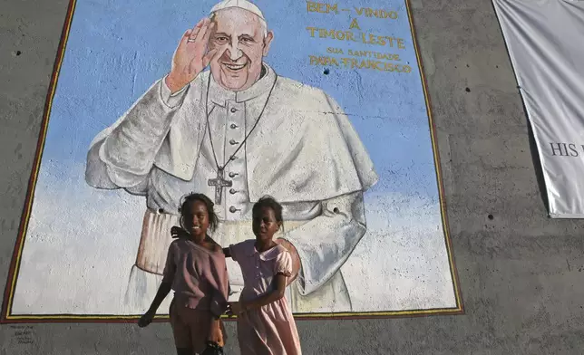 Girls stand in front a wall photo welcoming Pope Francis in Dili, East Timor on Tuesday, Sept. 3, 2024. (AP Photo/Firdia Lisnawati)