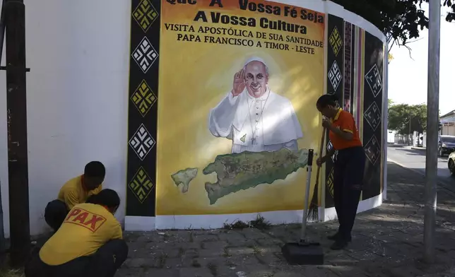 People clean a street next to a banner welcoming Pope Francis in Dili, East Timor Friday, Sept. 6, 2024. (AP Photo/Firdia Lisnawati)