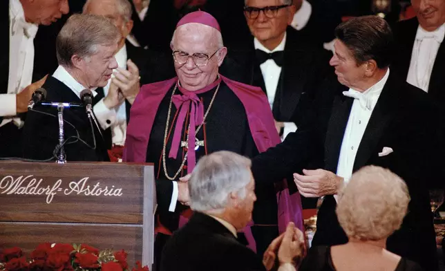 FILE - President Jimmy Carter shakes hands with his rival, Republican presidential nominee Ronald Reagan, at the Al Smith Foundation dinner at the Waldorf-Astoria in New York, Oct. 16, 1980. Archbishop John J. Maguire, center, looks on. (AP Photo/Richard Drew, File)