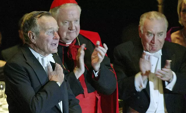 FILE - Former President George H.W. Bush, left, is applauded by Archbishop of New York Cardinal Edward Egan and former Governor of the State of New York Hugh L. Carey, right, after Bush spoke at the 59th annual Alfred E. Smith Memorial Foundation Dinner at the Waldorf Astoria hotel in New York, Thursday, Oct 21, 2004. (AP Photo/Stuart Ramson, File)