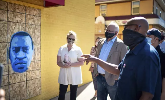 FILE - Minnesota Gov. Tim Walz, center right, listens to artist Seitu Jones, right, talk about his stencil of George Floyd, in St. Paul, Minn., Monday, June 8, 2020. (Glen Stubbe/Star Tribune via AP, Pool)