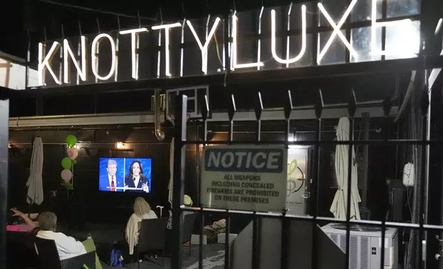 Patrons at the Knotty Luxe Bistro watch the presidential debate between Republican presidential nominee former President Donald Trump and Democratic presidential nominee Vice President Kamala Harris on an outdoor television Tuesday, Sept. 10, 2024, in Markham, Ill. (AP Photo/Charles Rex Arbogast)