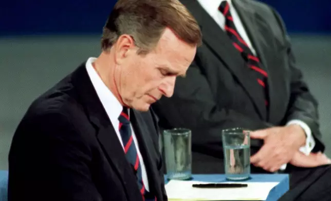 FILE - President George H.W. Bush looks at his watch during the 1992 presidential campaign debate with other candidates, Independent Ross Perot, top, and Democrat Bill Clinton, not shown, at the University of Richmond, Va., Oct. 15, 1992. (AP Photo/Ron Edmonds, File)