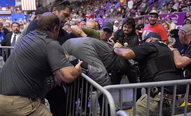 Police remove a man, center, who had climbed onto the media riser, as Republican presidential nominee former President Donald Trump speaks at a campaign event, Friday, Aug. 30, 2024, in Johnstown, Pa. (AP Photo/Alex Brandon)