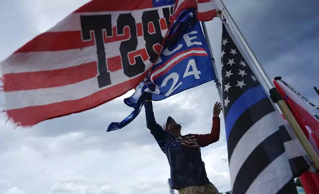 Jestin Nevarez, of Lake Worth, Fla., adjusts flags flying from his car as he shows support for Republican presidential nominee and former President Donald Trump outside of Trump's Mar-a-Lago estate, a day after an apparent assassination attempt, in Palm Beach, Fla., Monday, Sept. 16, 2024. (AP Photo/Rebecca Blackwell)