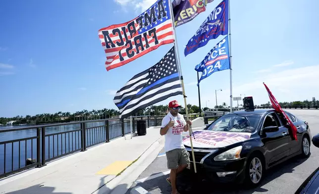 Justin Navarez, of Lake Worth, Fla. puts up flags on his vehicle outside of the Mar-a-Lago estate after the apparent assassination attempt of Republican presidential nominee and former President Donald Trump Monday, Sept. 16, 2024, in Palm Beach, Fla. (AP Photo/Lynne Sladky)