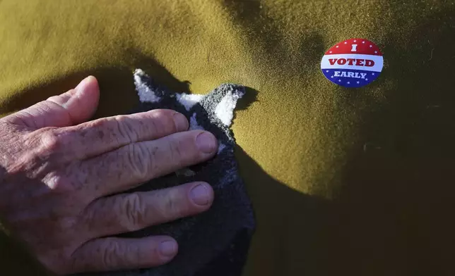 Minneapolis voter Scott Graham touches his heart while wearing an early voting sticker as he is interviewed at the City of Minneapolis early voting center, Friday, September 20, 2024, in Minneapolis, Minn. (AP Photo/Adam Bettcher)