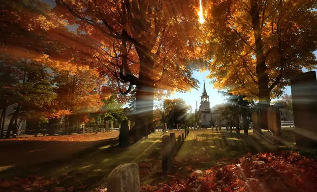 FILE - In this photo taken with a slow shutter speed, autumn's colors peak on hardwood trees in a cemetery near the Congregational Church, Monday, Oct. 10, 2016, in Cumberland, Maine. (AP Photo/Robert F. Bukaty, File)