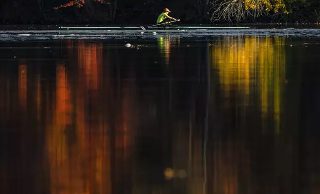 FILE - Fall foliage reflects on the Androscoggin River as Kathy Thorson rows a single scull, Oct. 12, 2021, in Brunswick, Maine. (AP Photo/Robert F. Bukaty, File)