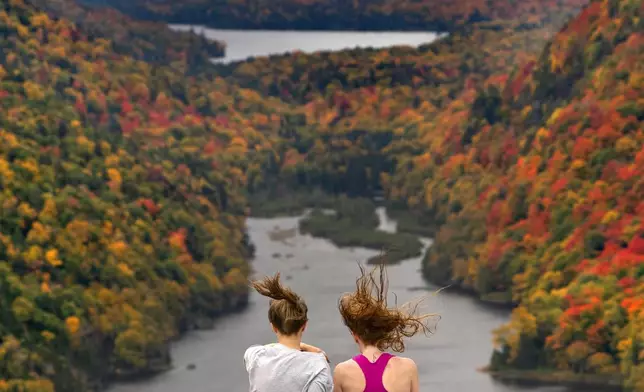 FILE - Wind whips the hair of two visitors taking in the view at the Indian Head vista overlooking Lower Ausable Lake in the Adirondacks, Sept. 27, 2020, near Keene Valley, N.Y. (AP Photo/Robert F. Bukaty, File)