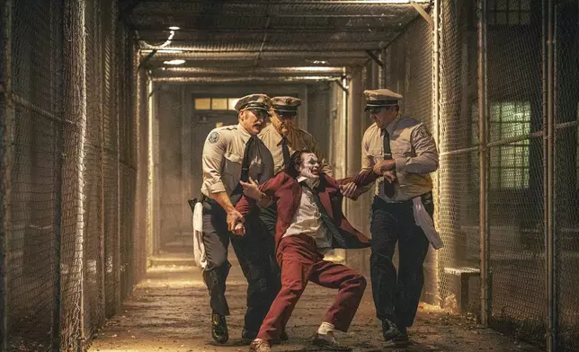 This image released by Warner Bros. Pictures shows Joaquin Phoenix, foreground center, and Brendan Gleeson, background center, in a scene from "Joker: Folie à Deux." (Niko Tavernise/Warner Bros. Pictures via AP)