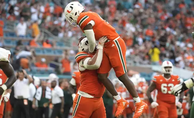 Miami offensive lineman Francis Mauigoa, left, lifts quarterback Cam Ward (1) after Ward threw a touchdown pass to running back Chris Johnson Jr. during the first half of an NCAA football game against Florida A&amp;M, Saturday, Sept. 7, 2024, in Miami Gardens, Fla. (AP Photo/Lynne Sladky)