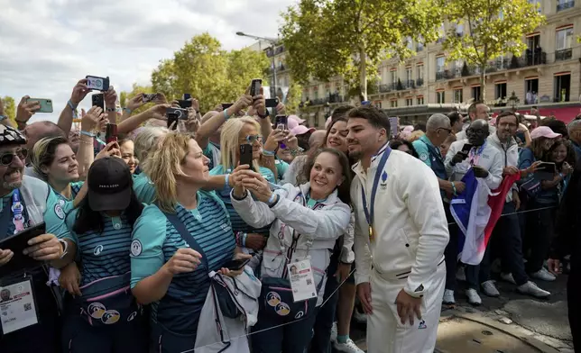 Antoine Dupont, gold medalist in Rugby 7s poses with olympic volunteers for a selfie on the day of a parade for all the French athletes who participated in the 2024 Olympics and Paralympics, Saturday, Sept. 14, 2024 in Paris. (AP Photo/Aurelien Morissard, Pool)