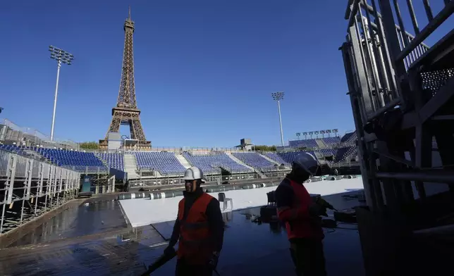 Workers remove grandstand seating as part of the dismantling of the Olympic venue the "Stade Tour Eiffel" with the Eiffel tower in the background in Paris, Friday, Sept. 13, 2024. (AP Photo/Michel Euler)