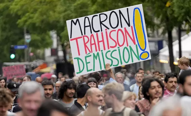 A demonstrator holds a poster which reads 'Macron treason resignation' during a protest, responding to a call from the far-left party who criticized as a power grab the president's appointment of a conservative new prime minister, Michel Barnier, in Paris, France, Saturday, Sept. 7, 2024. (AP Photo/Michel Euler)