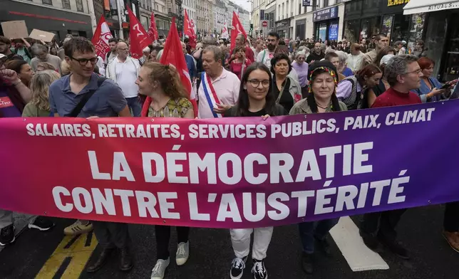 Demonstrators display a banner which reads 'democracy against austerity' during a protest, responding to a call from the far-left party who criticized as a power grab the president's appointment of a conservative new prime minister, Michel Barnier, in Paris, France, Saturday, Sept. 7, 2024. (AP Photo/Michel Euler)