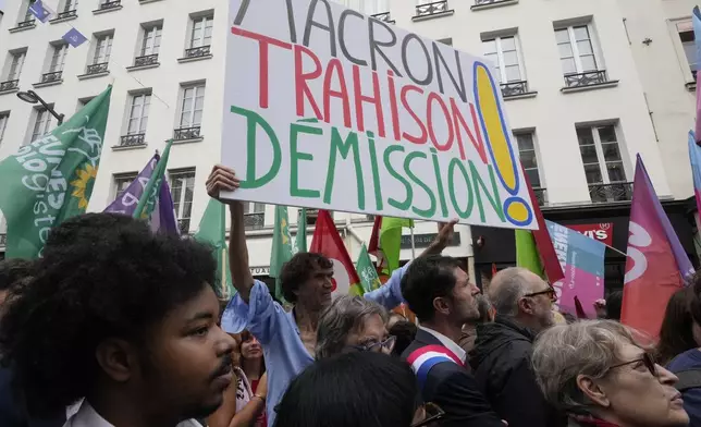 A demonstrator holds a poster which reads 'Macron treason resignation' during a protest, responding to a call from the far-left party who criticized as a power grab the president's appointment of a conservative new prime minister, Michel Barnier, in Paris, France, Saturday, Sept. 7, 2024. (AP Photo/Michel Euler)