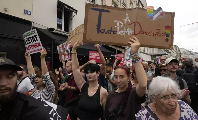 A demonstrator, on right, holds a placard which reads 'don't touch my democracy' during a protest, responding to a call from the far-left party who criticized as a power grab the president's appointment of a conservative new prime minister, Michel Barnier, in Paris, France, Saturday, Sept. 7, 2024. (AP Photo/Michel Euler)