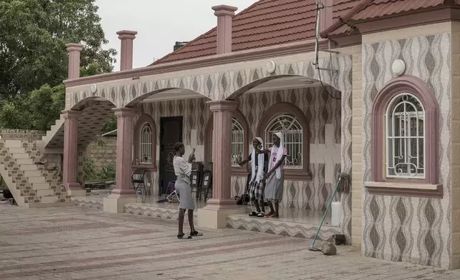 Teenagers record a TikTok video on the steps of a house owned by a migrant living in Seattle, U.S., in the village of Kaiaf, Gambia, on July 27, 2024. (AP Photo/Annika Hammerschlag)