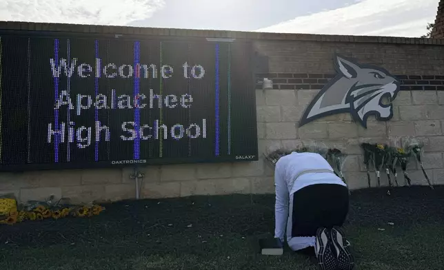 A person kneels in front of flowers that are placed outside the entrance to Apalachee High School on Thursday, Sept. 5, 2024 in Winder, Ga., a day after deadly shootings at the school. (AP Photo/Charlotte Kramon)