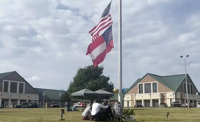 People gather at the flagpole outside the entrance to Apalachee High School on Thursday, Sept. 5, 2024 in Winder, Ga., a day after deadly shootings at the school. (AP Photo/Sharon Johnson)