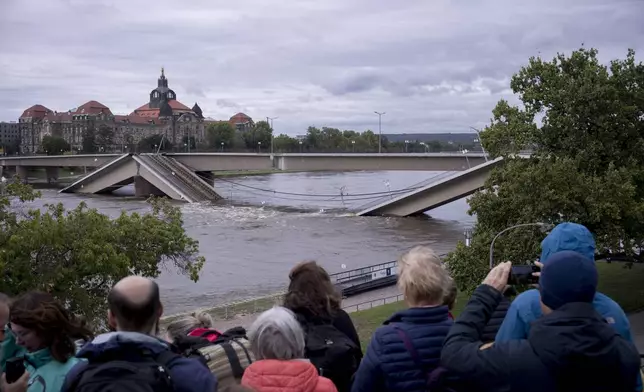 Spectators look at the partially collapsed Carolabrücke bridge over the Elbe, which is rising rapidly due to upcoming flood waters, in front of the state chancellery in Dresden, Germany, Sunday, September 15, 2024. (AP Photo/Markus Schreiber)