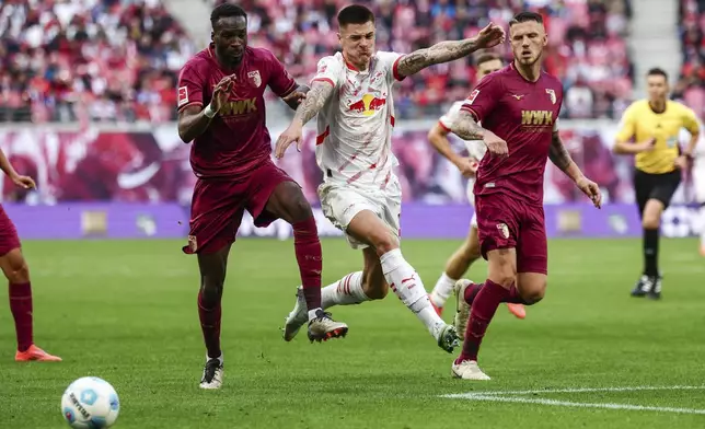 Leipzig's Benjamin Sesko, centre, challenges for the ball with Augsburg's Yusuf Kabadayi, left, and Chrislain Matsima during the German Bundesliga soccer match between RB Leipzig and FC Augsburg at the Red Bull Arena, in Leipzig, Germany, Sept. 28, 2024. (Jan Woitas/dpa via AP)