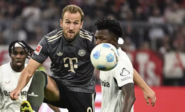 Munich's Harry Kane passes the ball past Leverkusen's Edmond Tapsoba during the German Bundesliga soccer match between Bayern Munich and Leverkusen at the Allianz Arena in Munich, Germany, Saturday, Sept. 28, 2024. (Lukas Barth-Tuttas/dpa via AP)