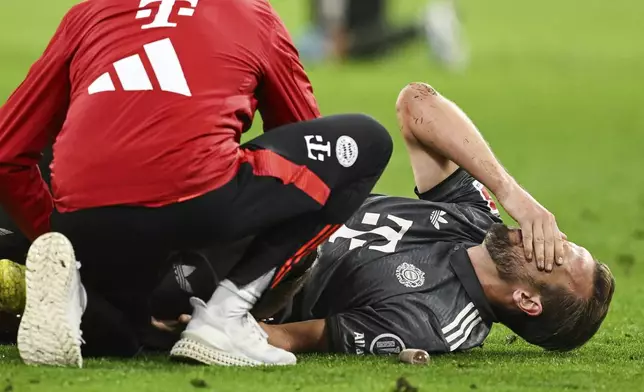 Munich's Harry Kane gets assistance as he lies on the pitch during the German Bundesliga soccer match between Bayern Munich and Leverkusen at the Allianz Arena in Munich, Germany, Saturday, Sept. 28, 2024. (Sven Hoppe/dpa via AP)