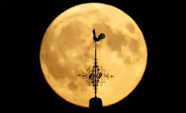 A weather vain on a church is silhouetted in front of the rising moon in Wehrheim near Frankfurt, Germany, Tuesday, Sept. 17, 2024. (AP Photo/Michael Probst)