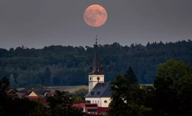 The full Harvest moon rises behind the church in Wehrheim near Frankfurt, Germany, Tuesday, Sept. 17, 2024. (AP Photo/Michael Probst)