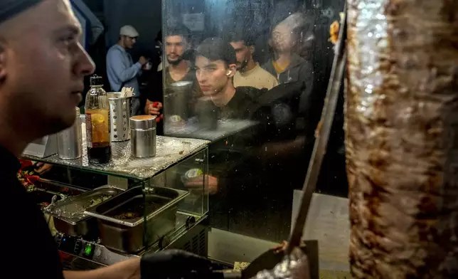 People stand in the line to buy doner kebab while the Turkish cook prepares the doner kebabs, in Berlin, Germany, Wednesday, Sept. 18, 2024. (AP Photo/Ebrahim Noroozi)