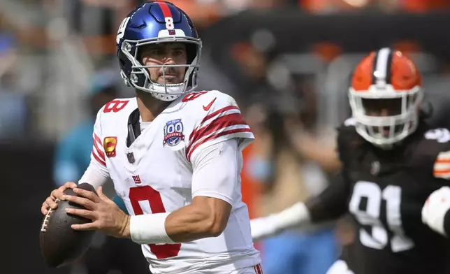 New York Giants quarterback Daniel Jones, left, looks to pass as Cleveland Browns defensive end Alex Wright (91) applies pressure during the first half of an NFL football game, Sunday, Sept. 22, 2024 in Cleveland. (AP Photo/David Richard)