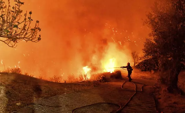 A firefighter tries to extinguish the flames near the village of Kallithea as fanned by strong winds raged uncontrolled despite the attempts of the authorities to stop the wildfire, some 149 kilometers (93 miles) west of Athens, Greece, in the region of Corinthia, late Sunday, Sept. 29, 2024. (AP Photo)