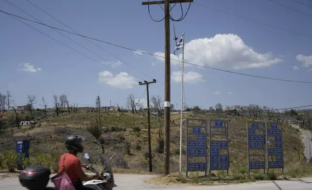 A man with a motorcycle passes Drosopigi village on Parnitha mountain which had been burned in an Aug. 2021 wildfire, in the outskirts of Athens, Friday, Aug. 23, 2024. (AP Photo/Thanassis Stavrakis)