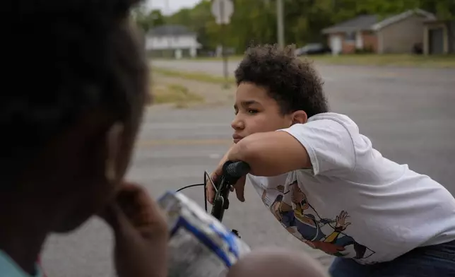 A kid leans on his bike handlebars as he gathers with neighborhood friends to sell Kool-Aid and Chips, Tuesday, Sept. 17, 2024, in Springfield, Ohio. Some were kept home from school because of the bomb threats at their schools, and if that happens again, they plan to be at the corner with Kool-Aid and chips again tomorrow. (AP Photo/Carolyn Kaster)