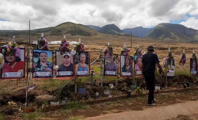 FILE - A visitor walks by photos of victims of the August 2023 wildfire at a memorial near the Lahaina Bypass highway on Saturday, July 6, 2024, in Lahaina, Hawaii. (AP Photo/Lindsey Wasson, File)