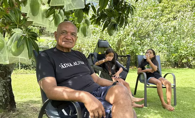 Randy Awo sits in his backyard with his granddaughters in Wailuku, Hawaii, on Thursday, July 18, 2024. As a Native Hawaiian Maui resident and a retired administrator in the state Department of Land and Natural Resources, Awo said he is concerned about storing debris from last year's deadly fire anywhere on the island. (AP Photo/Jennifer Sinco Kelleher)