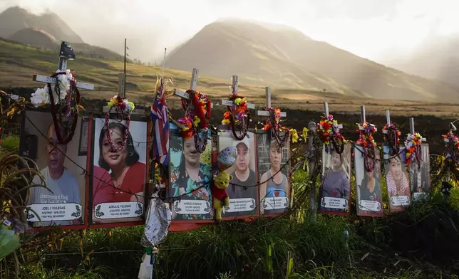 FILE - Photos of victims are displayed under white crosses at a memorial for victims of the August 2023 wildfire, above the Lahaina Bypass highway, Dec. 6, 2023, in Lahaina, Hawaii. (AP Photo/Lindsey Wasson, File)