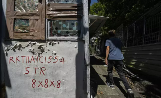 Villager Lo Yuet-ping walks past squatter registration info written on the walls of a house in Cha Kwo Ling village in east Kowloon, Hong Kong, Sunday, Aug. 25, 2024. (AP Photo/Chan Long Hei)