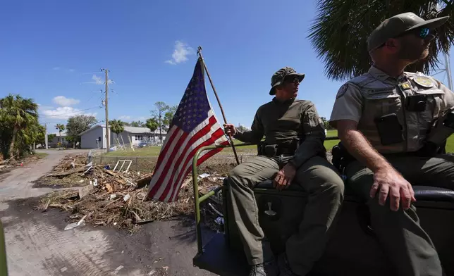 Officer Nate Martir, a law enforcement officer from the Florida Fish Wildlife and Conservation Commission, holds an American flag that was lying on the ground amid debris, while patrolling from a high water capable swamp buggy, in the aftermath of Hurricane Helene, in Cedar Key, Fla., Friday, Sept. 27, 2024. (AP Photo/Gerald Herbert)