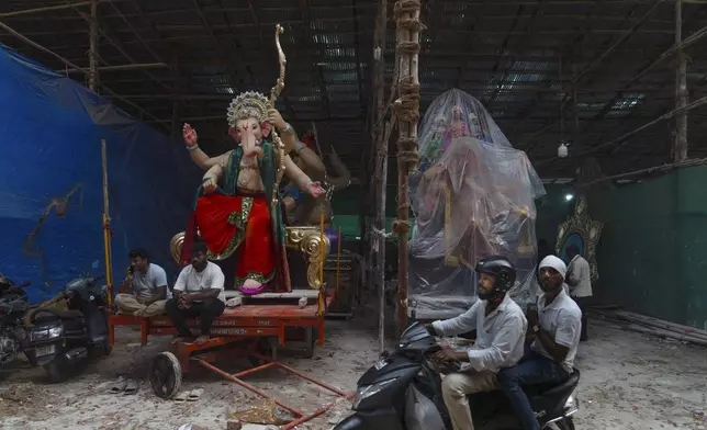 A scooterist drives past a workshop for idols of the elephant-headed Hindu god Ganesh ahead of Ganesh Chaturti festival in Mumbai, India, Wednesday, Sept. 4, 2024. (AP Photo/Rafiq Maqbool)